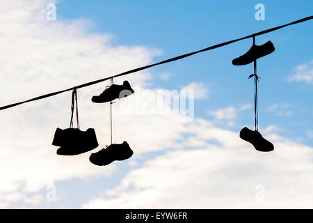 Silhouettes of shoes hanging on cable against sky. Stock Photo