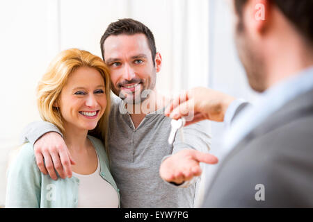 View of Real estate agent delivers keys of new house to young couple Stock Photo