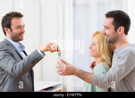 View of Real estate agent delivers keys of new house to young couple Stock Photo