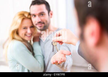 View of Real estate agent delivers keys of new house to young couple Stock Photo