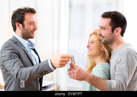 View of Real estate agent delivers keys of new house to young couple Stock Photo