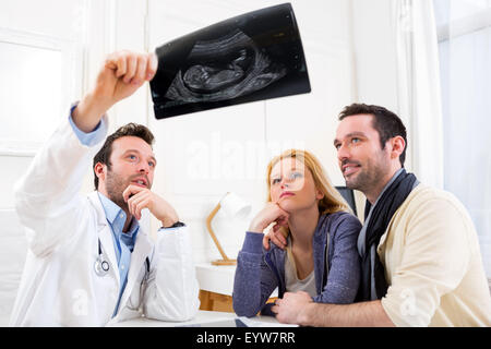 View of a Doctor shows an ultrasound to a young happy couple Stock Photo