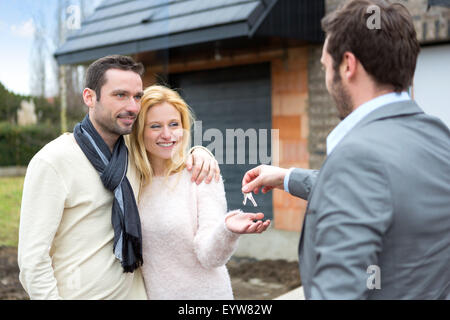 View of a Real estate agent delivers keys to young atractive couple Stock Photo