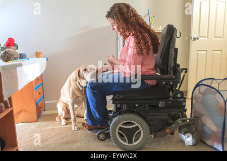 Woman with Muscular Dystrophy patting her service dog in her office Stock Photo