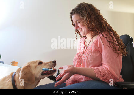 Woman with Muscular Dystrophy in her power chair working with her service dog to hand her items Stock Photo