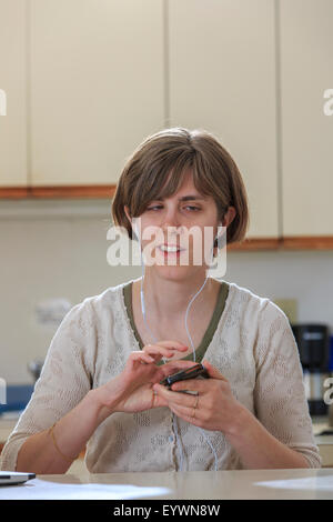 Blind woman using assistive technology ear plugs to listen to her cell phone Stock Photo