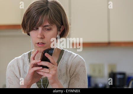 Blind woman using assistive technology ear plugs to listen to her cell phone Stock Photo