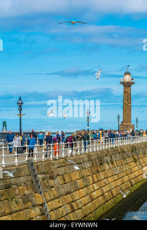 Tourists wearing winter coats on the West Pier in Whitby, on a cold but sunny July day. North Yorkshire Stock Photo