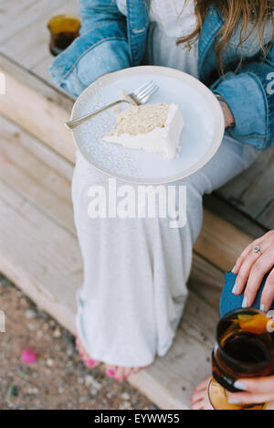 High angle view of a plate with a slice of cake balanced on a woman's knee. Stock Photo