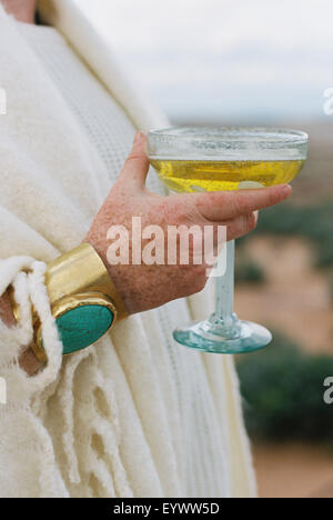 A woman wearing a golden bracelet with a large oval turquoise stone holding a glass. Stock Photo