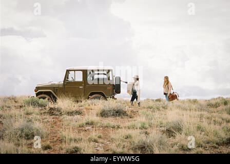 Two women by a jeep in open space, loading up for a road trip. Stock Photo