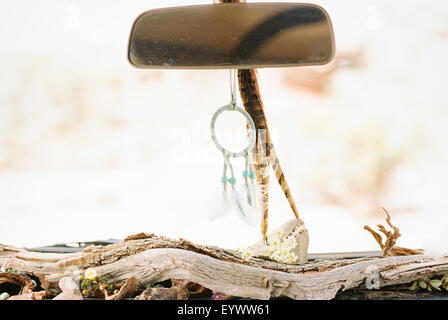 Close up of a car interior, driftwood on the dashboard, a dream catcher and feathers hanging from the rear view mirror.
