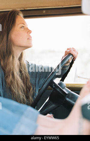 Barefoot woman resting her feet on the dashboard of a 4x4, a tattoo on her right foot, another woman driving. Stock Photo