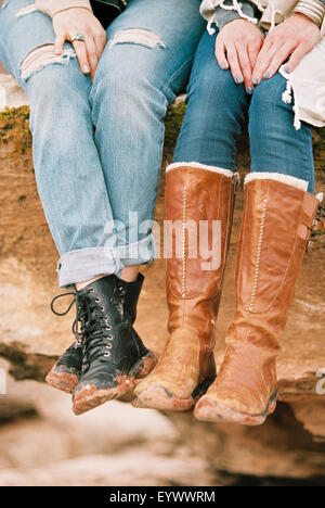 two women wearing leather boots sitting on a rock Stock Photo