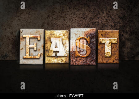 The word 'EAST' written in rusty metal letterpress type on a dark textured grunge background. Stock Photo