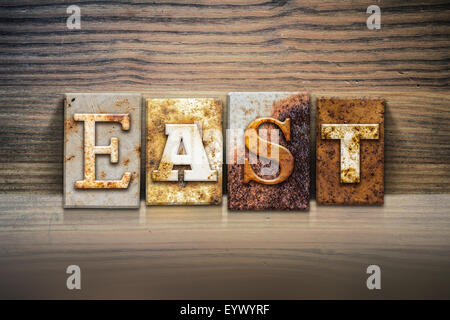 The word 'EAST' written in rusty metal letterpress type sitting on a wooden ledge background. Stock Photo