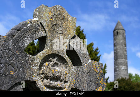 Cross in the foreground, with a soft focus view of the round tower, Glendalough, County Wicklow, Ireland. Stock Photo