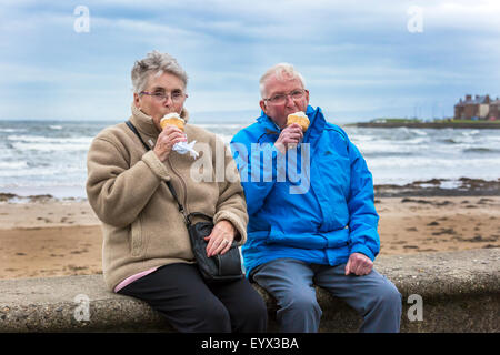 Unseasonably low temperatures and strong winds did not stop people enjoying a walk on the promenade at Troon, Ayrshire,Scotland, Donald Cameron and his wife Mary, aged 88 and 82, on a day trip from Falkirk are not put off by the bad weather and are enjoying an ice cream on the promenade. Stock Photo