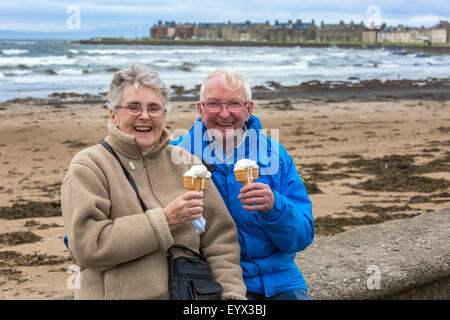 Unseasonably low temperatures and strong winds did not stop people enjoying a walk on the promenade at Troon, Ayrshire,Scotland, Donald Cameron and his wife Mary, aged 88 and 82, on a day trip from Falkirk are not put off by the bad weather and are enjoying an ice cream on the promenade. Stock Photo