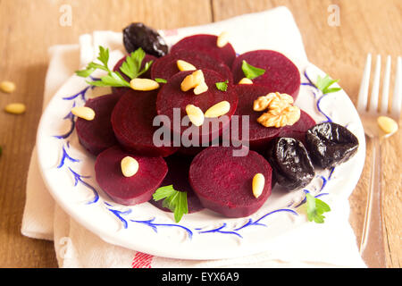 Boiled sliced beetroots (salad) on plate with pine nuts, walnuts, prunes (plumes) and parsley over rustic wooden table. Ingredie Stock Photo