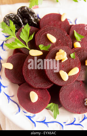 Boiled sliced beetroots (salad) on plate with pine nuts, walnuts, prunes (plumes) and parsley over rustic wooden table. Ingredie Stock Photo