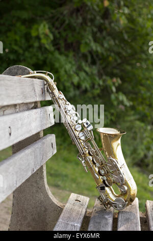 Summer Jazz saxophone in nature propped on park bench Stock Photo