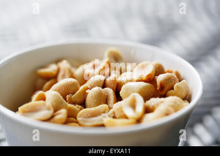 A small bowl of protein but sodium rich roasted salted peanuts presented as a snack in a small white bowl. Stock Photo