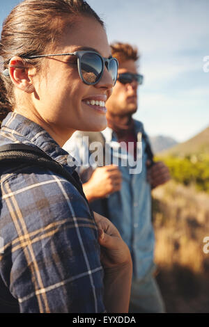 Close up image of young woman looking away smiling with young man in background. Hiker couple enjoying summer vacation in countr Stock Photo