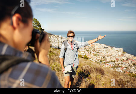 Outdoor shot of tourist couple enjoying nature and taking photo. Woman taking picture of boyfriend showing something with his ha Outdoor shot of tourist couple enjoying nature and taking photo. Woman taking picture of boyfriend showing something with his ha