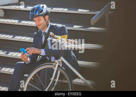 Businessman in suit with bicycle and helmet texting with cell phone on stairs Stock Photo