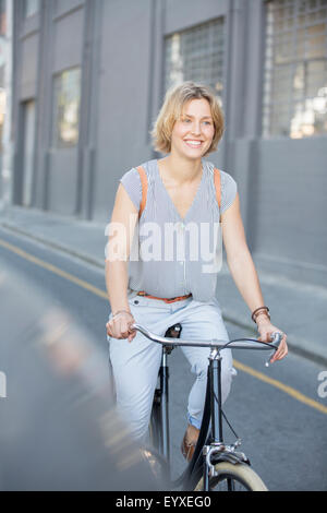 Smiling blonde woman riding bicycle on urban street Stock Photo