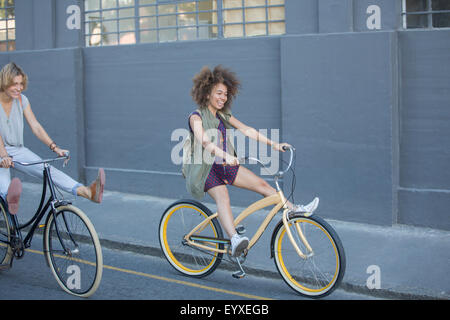 Playful women coasting on bicycles down urban street Stock Photo