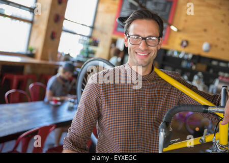Portrait smiling man with eyeglasses carrying bicycle in cafe Stock Photo