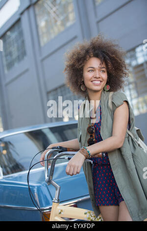 Smiling young woman with afro holding bicycle on urban street Stock Photo