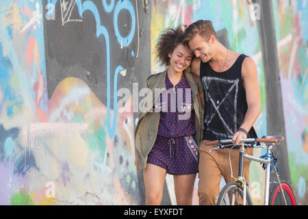 Couple hugging and walking with bicycle along urban graffiti wall Stock Photo
