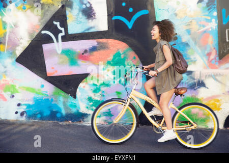 Woman riding bicycle along urban multicolor graffiti wall Stock Photo