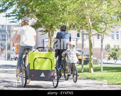 Families riding bicycles in sunny urban park Stock Photo