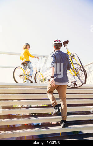 Man in helmet carrying bicycle up urban stairs Stock Photo