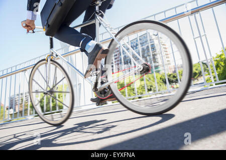 Low section businessman in suit riding bicycle on sunny urban sidewalk Stock Photo