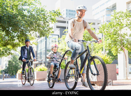 Mother and son in helmets riding tandem bicycle in urban park Stock Photo