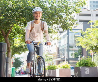 Portrait smiling young woman in helmet riding bicycle in urban park Stock Photo