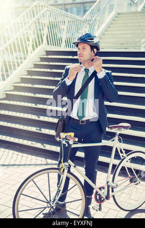 Businessman in suit with bicycle fastening helmet near urban stairs Stock Photo