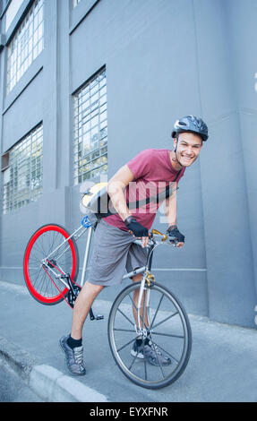 Portrait smiling bicycle messenger with helmet leaning forward on urban sidewalk Stock Photo