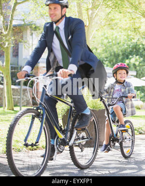 Businessman in suit and helmet riding tandem bicycle with son Stock Photo
