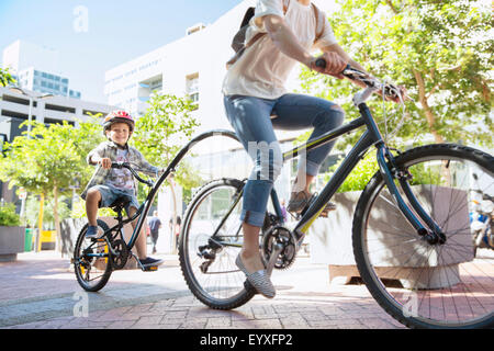 Son in helmet riding tandem bicycle with mother in urban park Stock Photo