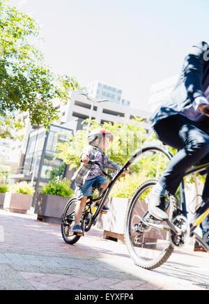 Son in helmet riding tandem bicycle with businessman father in sunny urban park Stock Photo