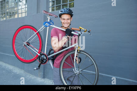 Portrait smiling young man carrying bicycle on urban sidewalk Stock Photo
