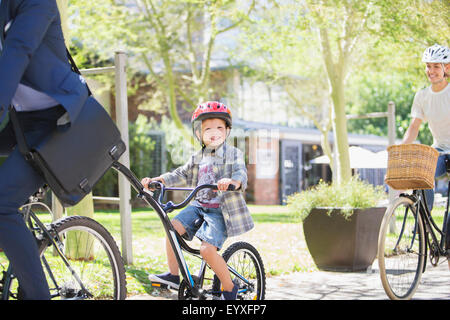 Portrait smiling boy in helmet riding tandem bicycle with father in park Stock Photo