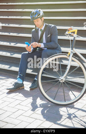 Businessman in suit and helmet texting with cell phone next to bicycle on sunny urban stairs Stock Photo