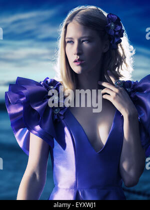 Beauty portrait of a young beautiful blond woman wearing a blue evening dress outdoors